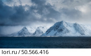 Majestic snow-capped mountains rise from the deep blue ocean under dramatic cloudy sky. Winter landscape with snowy rocks, overcast sky and sea in the Lofoten islands, Norway. Nature. Arctic scenery. Scenic snow-capped mountains emerge from the deep blue sea beneath a dramatic, cloudy sky, forming a stunning winter scene in the lofoten islands, norway. Стоковое фото, агентство Ingram Publishing / Фотобанк Лори