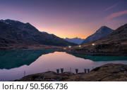 Sunset casts a serene glow on mountain peaks mirrored in a tranquil alpine lake in autumn. Lake Bianco, Switzerland in fall. Landscape with mountains, reflection in water, purple and orange sky. Dusk. Стоковое фото, агентство Ingram Publishing / Фотобанк Лори