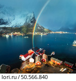 Aerial view of snowy mountains, colorful rainbow, blue sea and traditional red rorbuer houses in Reine at sunset. Winter landscape. Lofoten island, Norway. Top drone view of rorbu, fjord, rock in snow. Стоковое фото, агентство Ingram Publishing / Фотобанк Лори