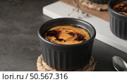 Creme brulee in a black ramekin with a caramelized sugar top, placed on a woven coaster, set against a dark background with a spoon nearby. Стоковое фото, агентство Ingram Publishing / Фотобанк Лори