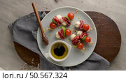 Caprese skewers with cherry tomatoes, mozzarella, basil, and salami on a plate with a small bowl of olive oil and balsamic vinegar, garnished with herbs. Стоковое фото, агентство Ingram Publishing / Фотобанк Лори