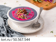 Purple soup with pink swirl, topped with pecans and rosemary, in a white speckled bowl on a matching plate, with a spoon and gray cloth nearby. Стоковое фото, агентство Ingram Publishing / Фотобанк Лори