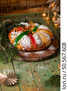 A traditional holiday sweet bread dusted with powdered sugar and adorned with candied fruits and green citrus peel, served on a rustic wooden board with pine branches. Стоковое фото, агентство Ingram Publishing / Фотобанк Лори