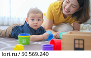 A tiny child cheerfully plays with toys on the floor of the living room with mom. Стоковое фото, агентство Ingram Publishing / Фотобанк Лори