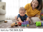 A tiny child cheerfully plays with toys on the floor of the living room with mom. Стоковое фото, агентство Ingram Publishing / Фотобанк Лори