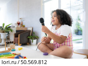 A tiny girl sits on a toy table, clutching a microphone, and sings cheerfully in the living room. Стоковое фото, агентство Ingram Publishing / Фотобанк Лори