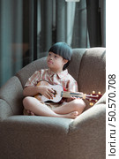 A special child plays the ukulele on a armchair in the living room of the house. Стоковое фото, агентство Ingram Publishing / Фотобанк Лори