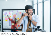 Portrait of smiling businessman riding electric scooter in office with colleague in background. Стоковое фото, агентство Ingram Publishing / Фотобанк Лори