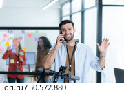 Portrait of smiling businessman talking on mobile phone while colleague using scooter in office. Стоковое фото, агентство Ingram Publishing / Фотобанк Лори