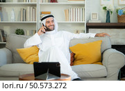 Portrait of a smiling Arabian man holding a glass of champagne and using mobile phone at home. Стоковое фото, агентство Ingram Publishing / Фотобанк Лори