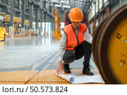Female worker in safety vest and hardhat sitting on floor in a skytrain repair station, Using blueprints to inspect train wheels. Стоковое фото, агентство Ingram Publishing / Фотобанк Лори