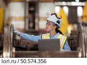 Railway technician in uniform and helmet inspect the train wheels removed from the locomotives in the train workshop. Стоковое фото, агентство Ingram Publishing / Фотобанк Лори