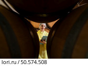 Smiling female winemaker in yellow uniform standing in cellar of winery. Стоковое фото, агентство Ingram Publishing / Фотобанк Лори