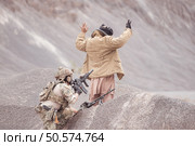 A Taliban soldier stands with a machine gun, Raise hands in surrender to the allied soldiers, In the desert mountain terrain battlefield. Стоковое фото, агентство Ingram Publishing / Фотобанк Лори