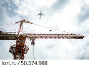 Tower crane in at construction site with air plane on sky in the background. Стоковое фото, агентство Ingram Publishing / Фотобанк Лори