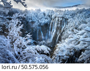 Aerial drone view of amazing waterfall and snowy forest at sunset. Winter fairytale in Plitvice Lakes, Croatia. Top view of white snow-covered frozen trees, waterfall, house, clouds on cold winter day. Стоковое фото, агентство Ingram Publishing / Фотобанк Лори