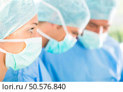 Hospital - surgery team in the operating room or Op of a clinic operating on a patient, perhaps it’s an emergency a assistant holding a cotton swap forceps. Surgeons operating patient in operation theater. Стоковое фото, агентство Ingram Publishing / Фотобанк Лори