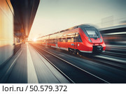 Beautiful railway station with modern high speed red commuter train with motion blur effect at colorful sunset in Nuremberg, Germany. Railroad with vintage toning. Стоковое фото, агентство Ingram Publishing / Фотобанк Лори