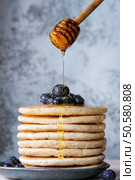 Pancakes with fresh blueberries in blue ceramic plate, and flowing honey from wooden honey dipper, served on white tablecloth with blue textured background.. Pancakes with fresh berries. Стоковое фото, агентство Ingram Publishing / Фотобанк Лори