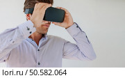 Close up shot of young man wearing virtual reality goggle against grey background. Caucasian male using VR goggle.. Man wearing virtual reality goggle. Стоковое фото, агентство Ingram Publishing / Фотобанк Лори