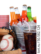 Picnic table ready for a summertime picnic. Cold soda bottles in a bucket full of ice, plastic cups and a full glass of cola with straw, baseball equipment and chips over a white background. Стоковое фото, агентство Ingram Publishing / Фотобанк Лори