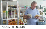 Uncertain mature male buyer choosing a package of flakes in grocery shop. Стоковое видео, видеограф Яков Филимонов / Фотобанк Лори