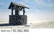 A brick water well with a wooden roof and bucket attached to a rope in a flat barren landscape with a blue sky background. Стоковое фото, агентство Ingram Publishing / Фотобанк Лори