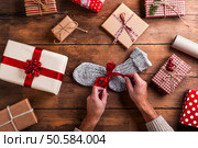 Man unwrapping Christmas present laid on a wooden table background. Man holding Christmas presents. Стоковое фото, агентство Ingram Publishing / Фотобанк Лори