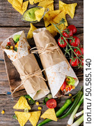 Mexican style dinner. Two papered tortillas burrito with beef and vegetables served with vegetables, nachos chips and guacomole sauce over old wooden background. Flat lay. Tortillas and nachos. Стоковое фото, агентство Ingram Publishing / Фотобанк Лори