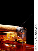 Lit Cigar resting on Glass of Whiskey and Ice cubes with wisp of smoke and black background. Стоковое фото, агентство Ingram Publishing / Фотобанк Лори
