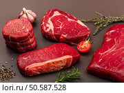 Set of various steaks with classic spices and herbs. Fresh raw meat cuts includes ribeye, eye round, flank and striploin steaks. Black stone concrete background, flat lay, close up. Стоковое фото, агентство Ingram Publishing / Фотобанк Лори