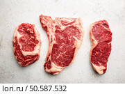 Variety of Fresh Raw Black Angus Prime Meat Steaks T-bone, New York, Ribeye and seasoning on white background, top view. Variety of Raw Meat Steaks. Стоковое фото, агентство Ingram Publishing / Фотобанк Лори