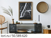 Modern scandinavian living room interior with mock up poster frame, design commode, leaf in vase, rattanarmchair, book and elegant accessories in stylish home decor. Template. . Стоковое фото, агентство Ingram Publishing / Фотобанк Лори