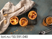 Three freshly baked Portuguese custard tarts on a cooling rack with a linen cloth and cinnamon ready to be sprinkled. Стоковое фото, агентство Ingram Publishing / Фотобанк Лори
