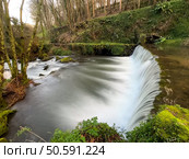 Water cascades over a stone weir, creating a mesmerizing scene near Cascata do Outeiro. The long exposure captures the movement of the water, creating a sense of tranquility in Oliveira de Azemeis. Стоковое фото, агентство Ingram Publishing / Фотобанк Лори