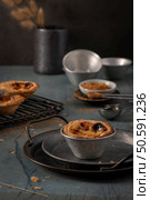 Rustic scene with Portuguese custard tarts in metal molds on a dark surface, surrounded by baking tools and ingredients, creating a cozy, homemade feel. Стоковое фото, агентство Ingram Publishing / Фотобанк Лори