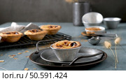 Four Portuguese custard tarts one on a metal tray others on a rack with cinnamon measuring spoons and decorative grasses nearby. Стоковое фото, агентство Ingram Publishing / Фотобанк Лори