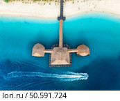Aerial view of bungalow, boat in blue sea at sunset in summer. Restaurant on the ocean. Top drone view of wooden hotel, azure water, white sandy beach, palm trees. Luxury resort in Kendwa, Zanzibar. Стоковое фото, агентство Ingram Publishing / Фотобанк Лори