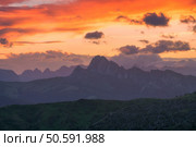 Colorful landscape with orange sky and silhouettes of mountain ranges at sunset. The warm hues of a breathtaking sunset paint the sky over the rugged peaks of the italian dolomites. Nature background. Стоковое фото, агентство Ingram Publishing / Фотобанк Лори