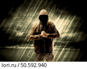An incognito hooded stalker standing in the rain with his back in front of dark scary landscape concept. Стоковое фото, агентство Ingram Publishing / Фотобанк Лори