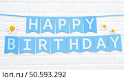 A cheerful blue banner spelling out "Happy Birthday" adorned with white daisy cutouts, set against a white brick background. Стоковое фото, агентство Ingram Publishing / Фотобанк Лори