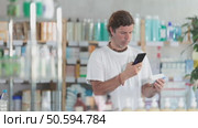 European man in summer clothes holds a mobile phone and scans the barcode on a package of ointment at a pharmacy. Buyer uses a non-cash method of payment for purchases. Стоковое видео, видеограф Яков Филимонов / Фотобанк Лори