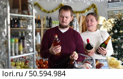 Happy young married couple choosing alcohol in grocery section of supermarket to celebrate Christmas. Стоковое видео, видеограф Яков Филимонов / Фотобанк Лори