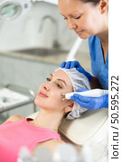 Experienced cosmetologist in rubber gloves does rf-lifting procedure on face for girl, smoothes wrinkles and tightens skin with use of electric hydrogen oxygen facial beauty machine in spa center. Стоковое фото, фотограф Яков Филимонов / Фотобанк Лори