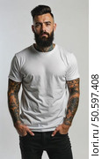 Attractive brutal tattooed bearded guy poses in black jeans and blank white t-shirt from premium thin summer cotton, isolated on white mockup background. Стоковое AI-видео, аниматор Sergey Grishin / Фотобанк Лори