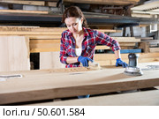 During manufacturing, woman employee grinds surface of wooden board, gives smoothness to surface. Стоковое фото, фотограф Яков Филимонов / Фотобанк Лори