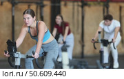 Athletic woman in top and leggings at cycling training. Client of the gym at a group workout on an exercise bike. Стоковое видео, видеограф Яков Филимонов / Фотобанк Лори