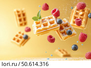 Golden Belgian waffles float in a vibrant yellow space. Topped with berries and mint, they glisten with honey, creating a lively and bold culinary work of art. Стоковое AI-изображение, AI-художник Nart / Фотобанк Лори