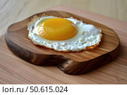 Fried egg resting on rustic wooden board displaying culinary simplicity. Стоковое AI-изображение, AI-художник Иван Рябоконь / Фотобанк Лори