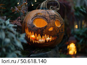 Halloween pumpkin glowing with candles in a spooky garden. Стоковое AI-изображение, AI-художник Иван Рябоконь / Фотобанк Лори
